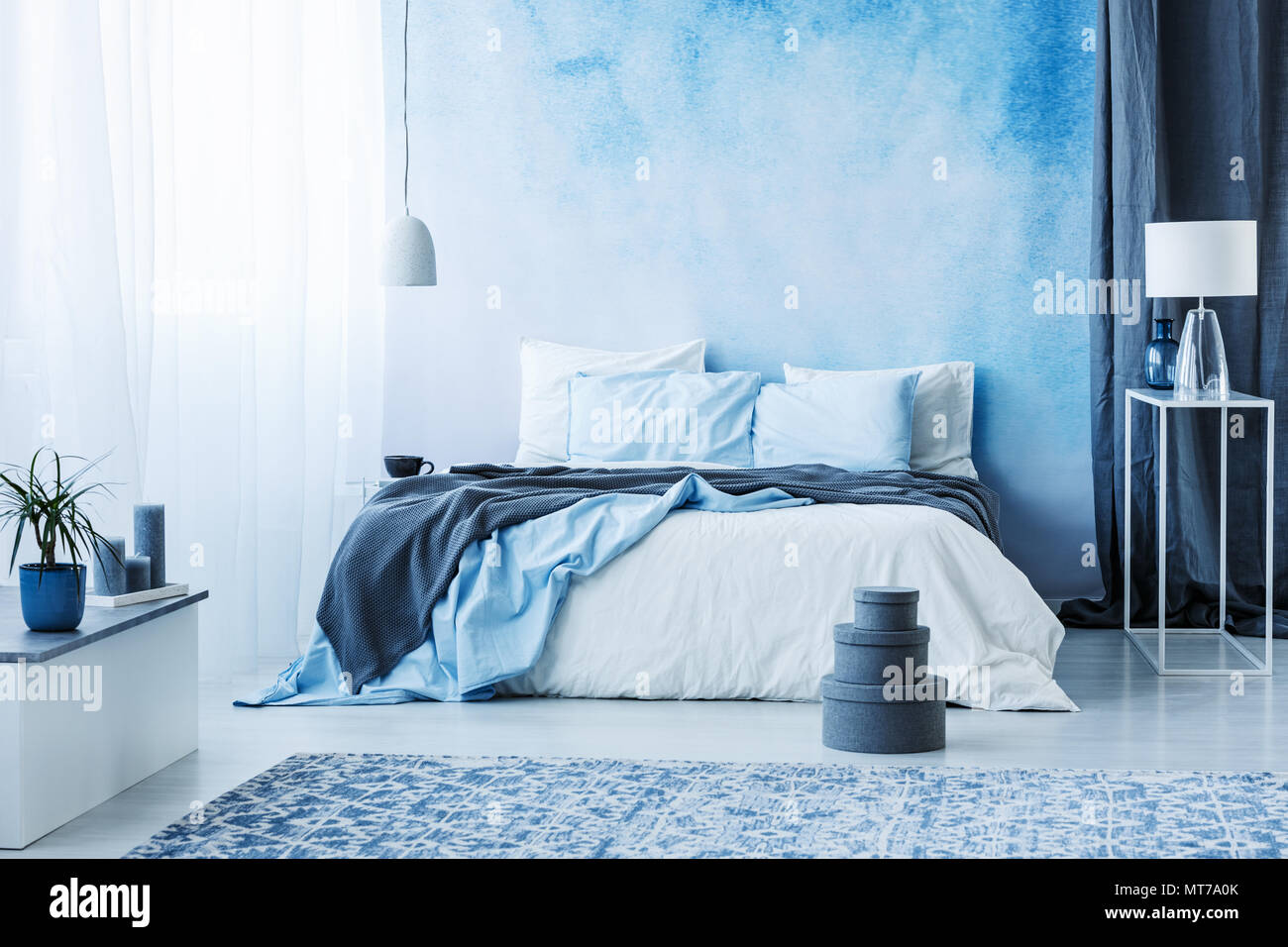 Grey boxes next to bed with blue bedding in bedroom interior with white ...