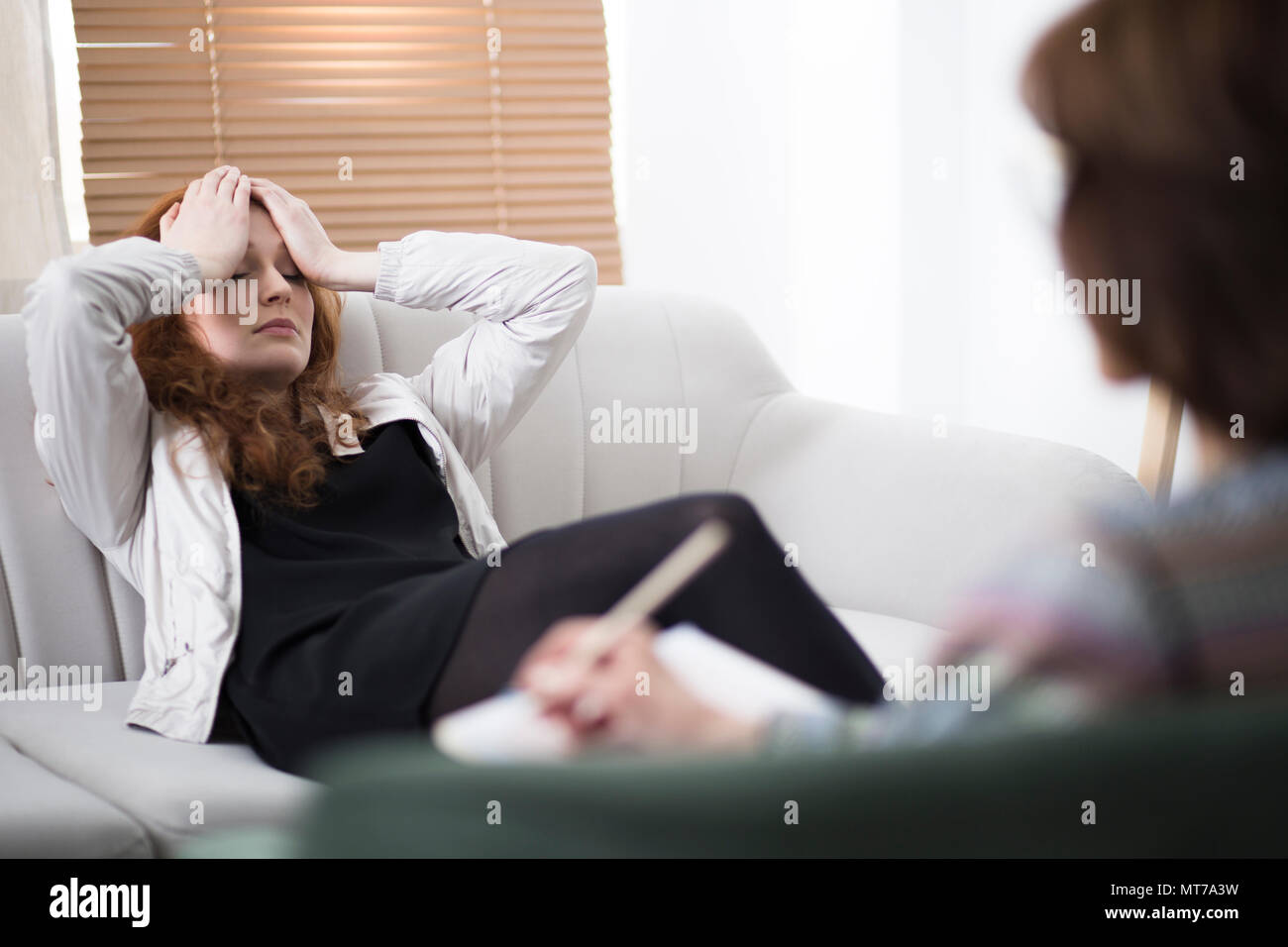 Depressed woman holding her head while sitting on a couch in a psychiatrist office Stock Photo
