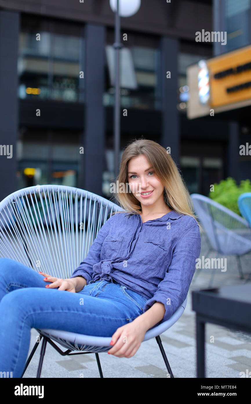 Smiling girl sitting in chair with building background Stock Photo - Alamy