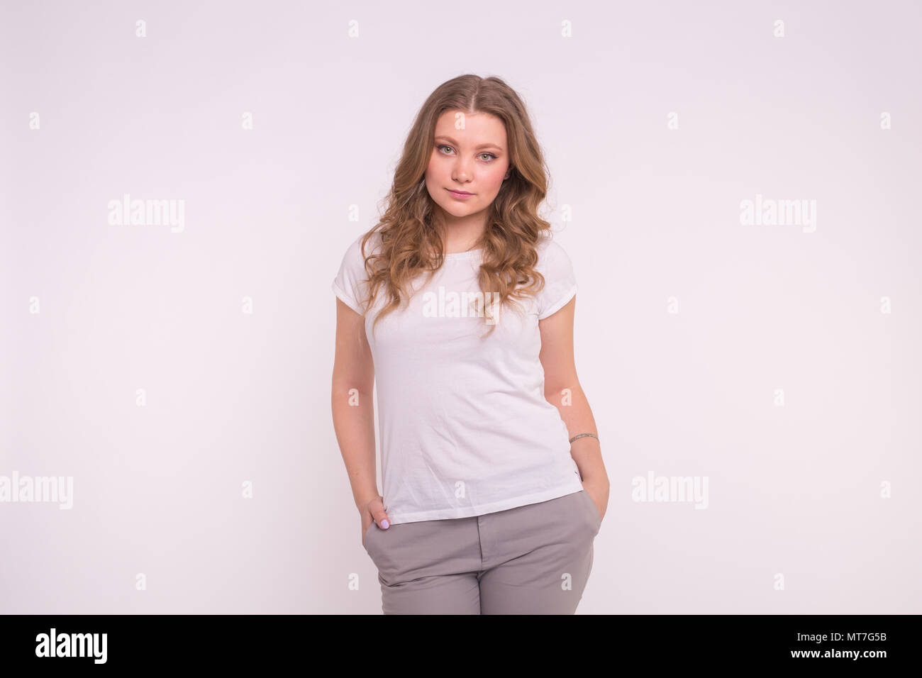 Young woman standing with hands in pockets, wearing white tshirt with ...