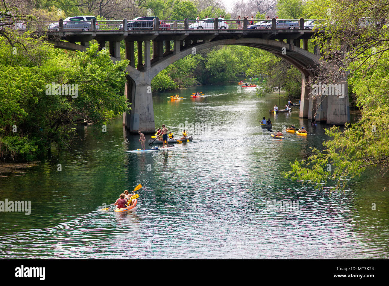 Young people using paddle boards, colorful canooes & kayacs, bridge crossing Barton Creek,  Colorado River, Zilker Park. Stock Photo
