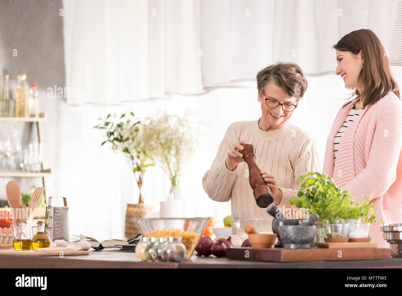 Smiling granddaughter and grandmother cooking in modern kitchen Stock Photo