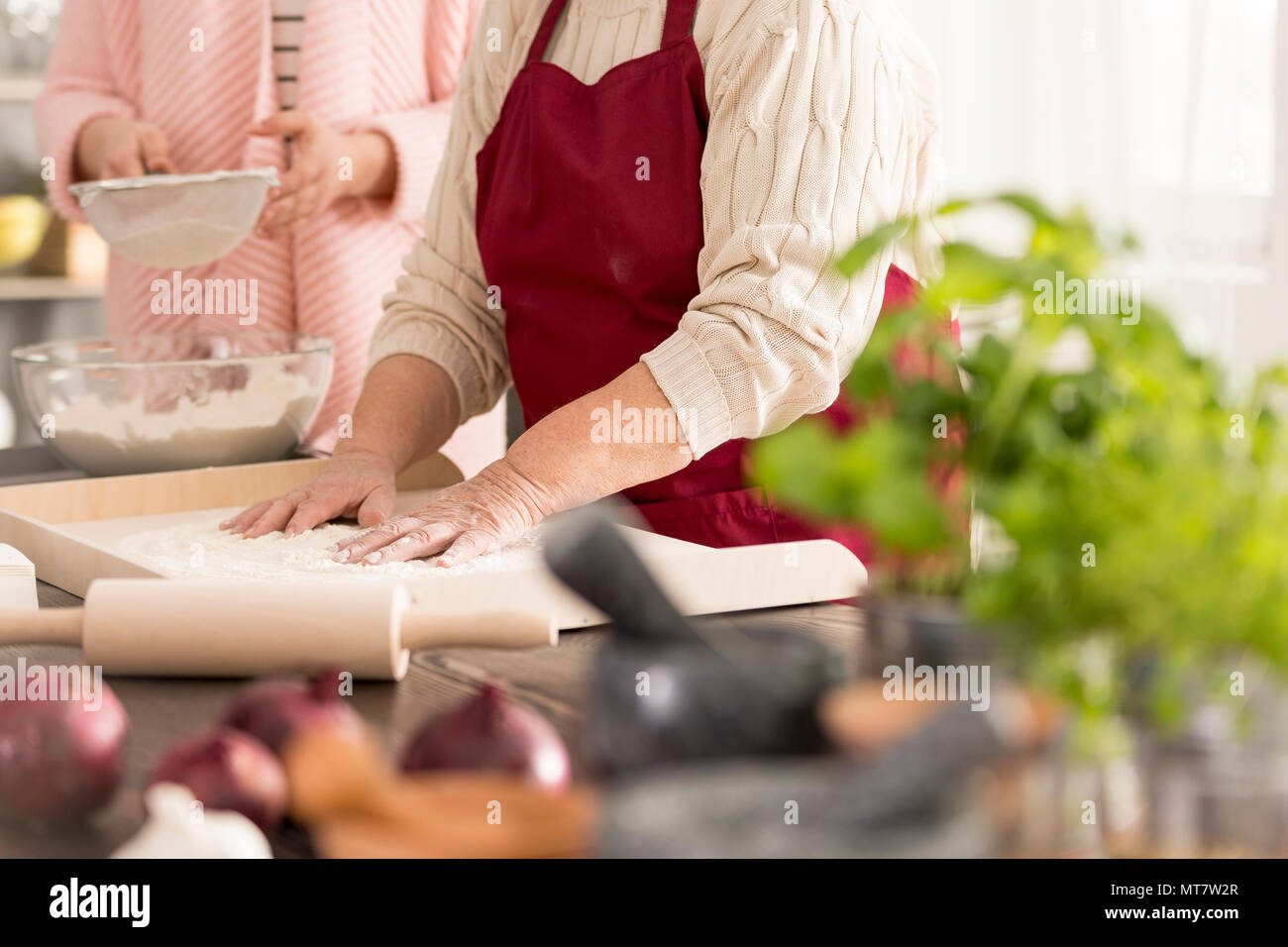 Old woman standing in a kitchen and baking a cake Stock Photo