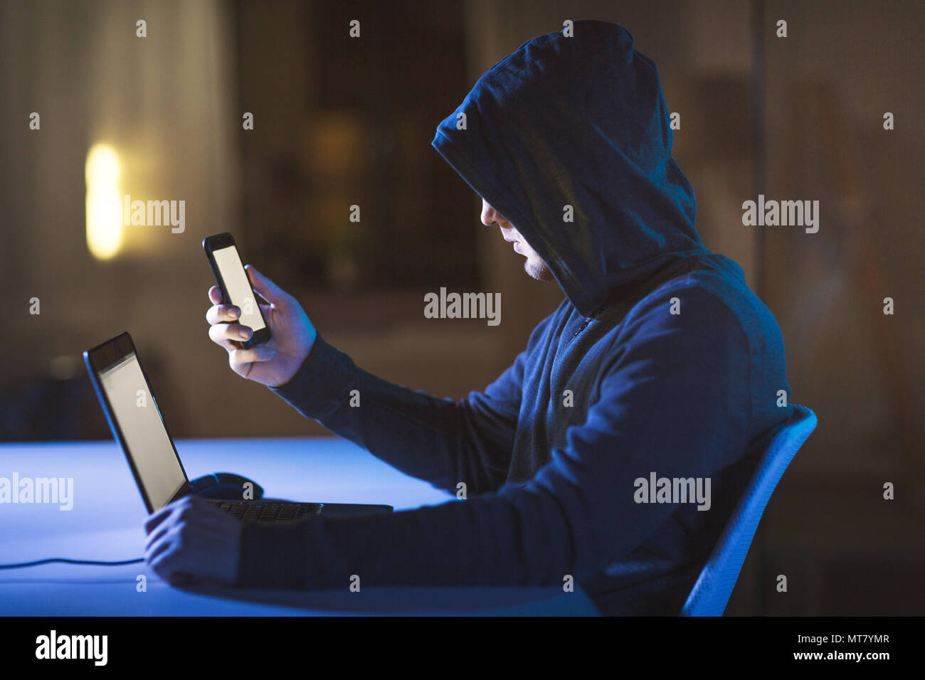 hacker with laptop and smartphone in dark room Stock Photo - Alamy
