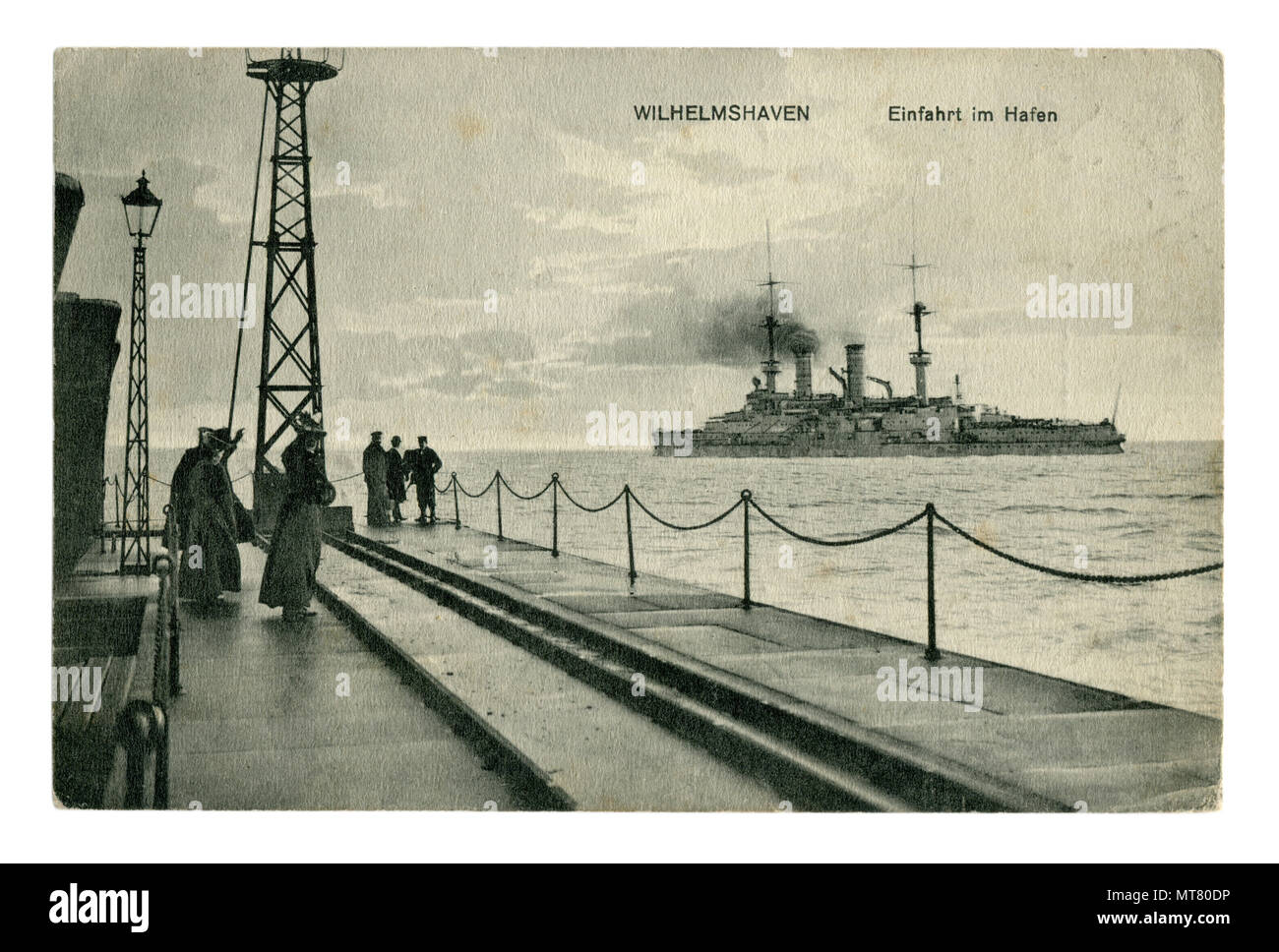 German historical photo postcard:  Pier at the entrance to the Harbor of Wilhelmshaven. Women and men look at the warship. world war one 1914-1918. Stock Photo