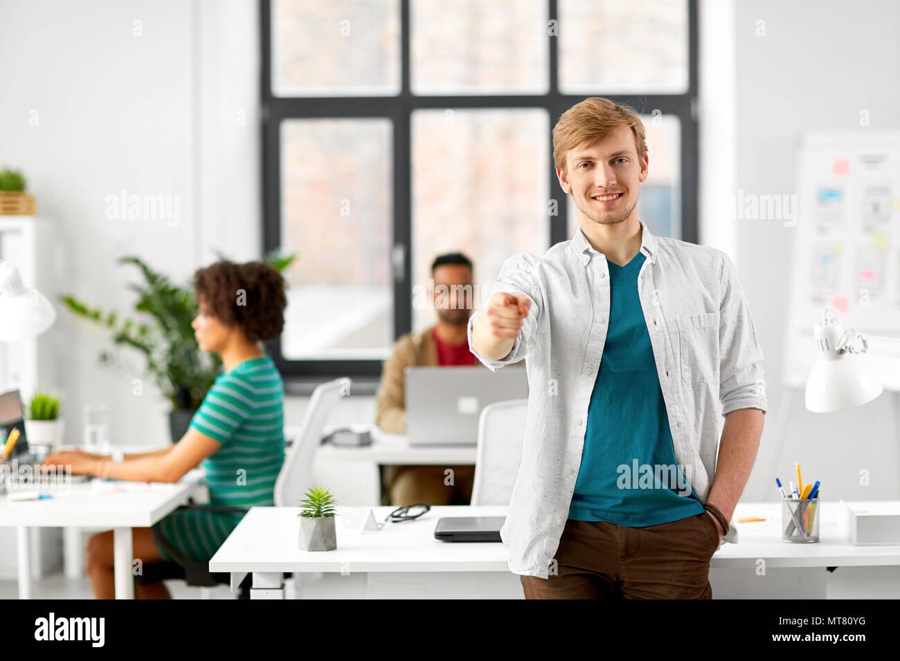 happy smiling man pointing finger at you at office Stock Photo