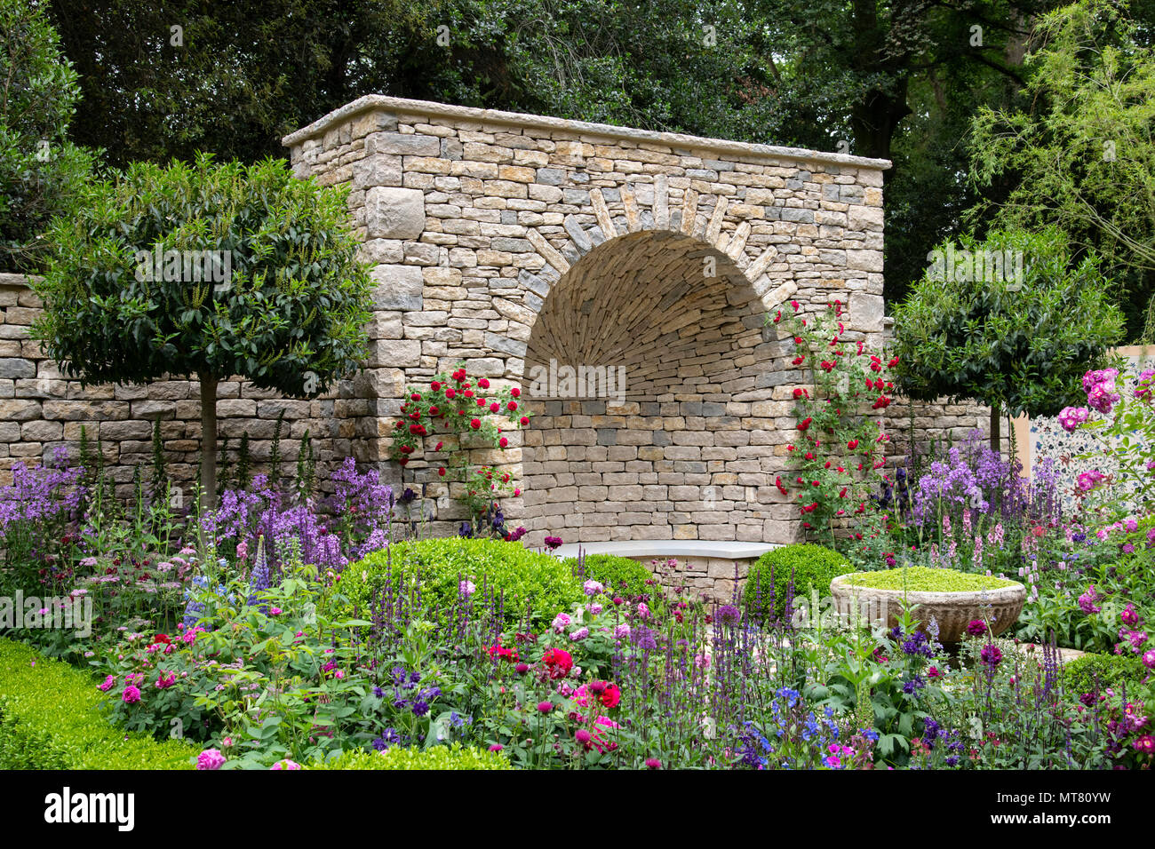 A dry stone niche surrounded by multi-coloured plants in The Claims Guys-A Very English Garden at The RHS Chelsea Flower Show 2018, London, UK Stock Photo