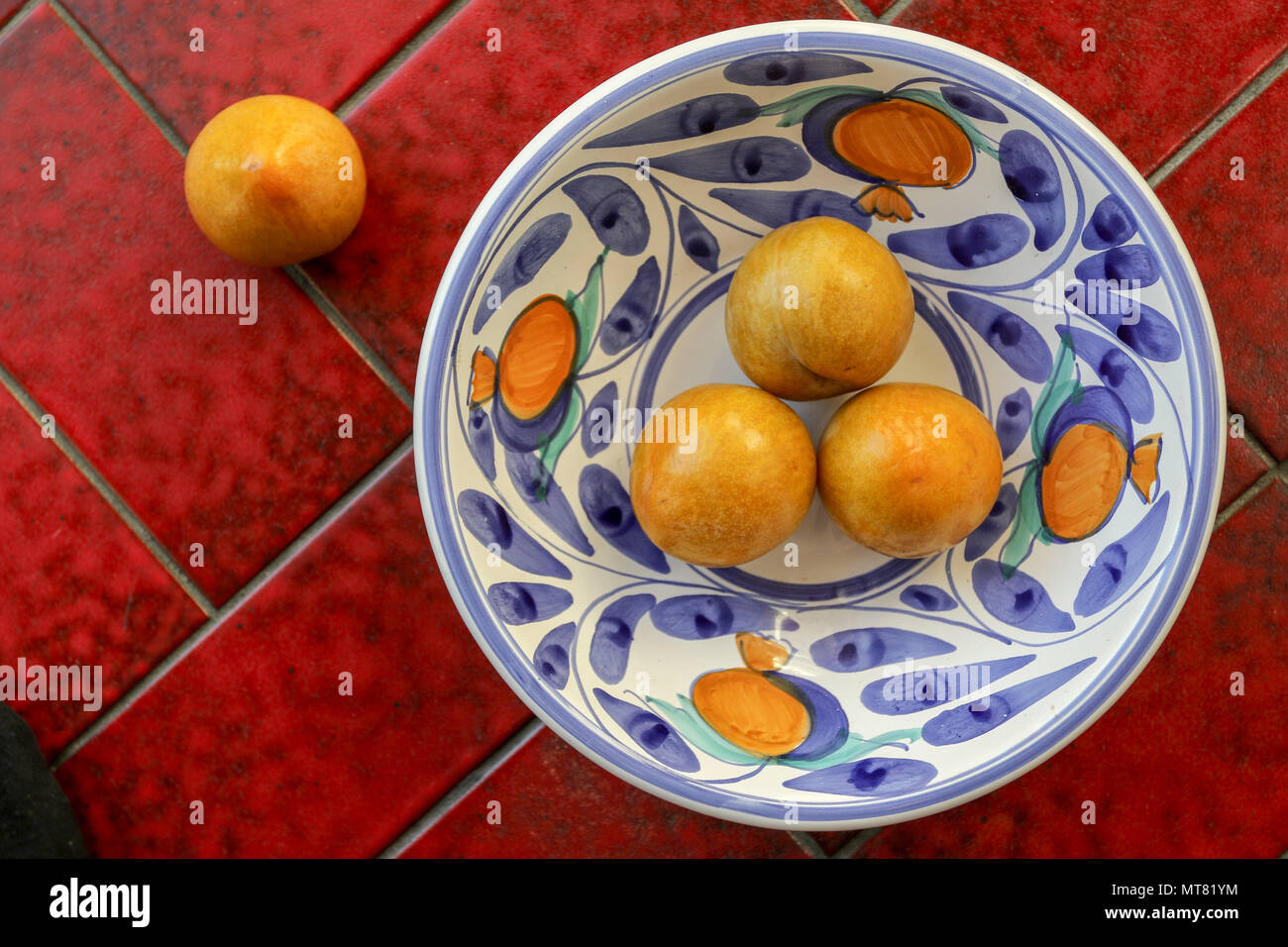 Yellow plums in white and blue coloured bowl on a red tile background Stock Photo