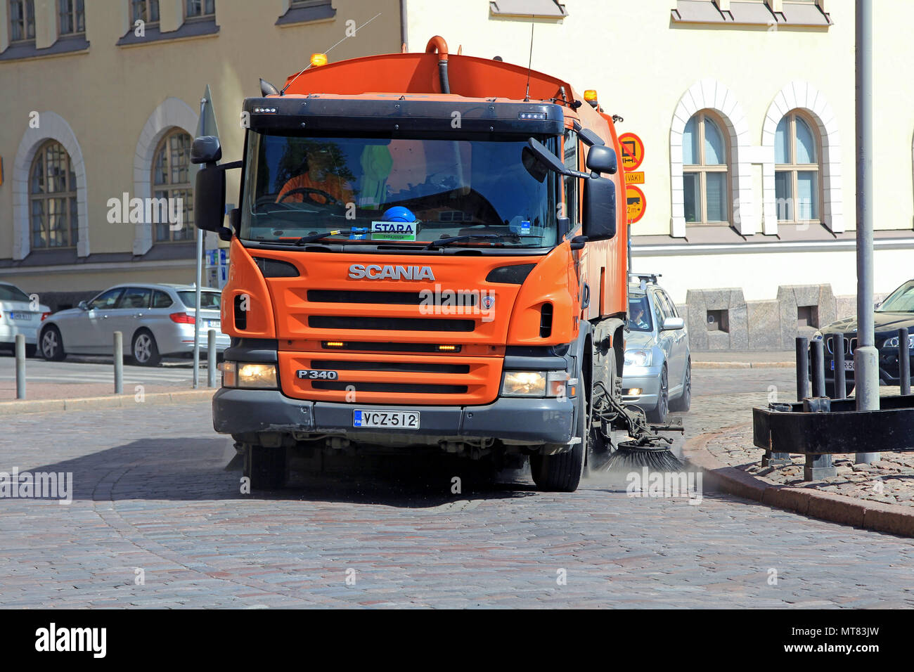 Orange Scania P340 road sweeper cleans city street among traffic on a sunny day of spring in Helsinki, Finland - May 24, 2018. Stock Photo