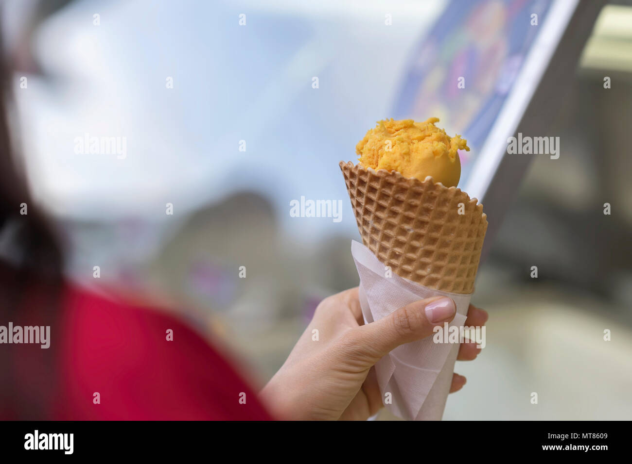 Ball of fruit ice cream orange color in waffle cone, Female hand. Popular delicacies for adults and children. Selective focus. Real scene Stock Photo