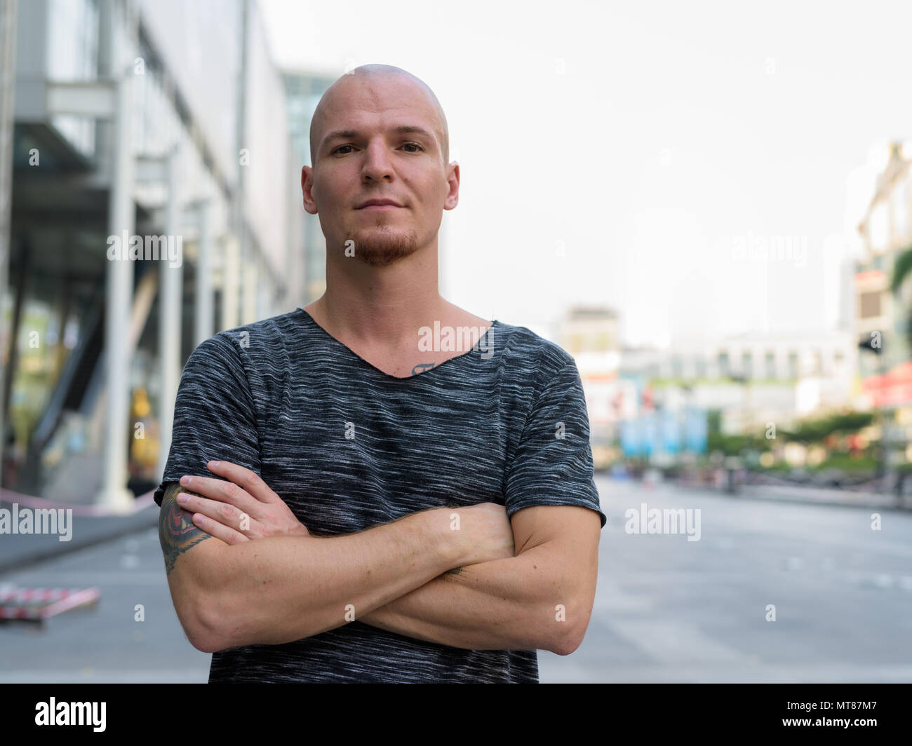 Young handsome bald man with arms crossed outside of the mall in Stock Photo