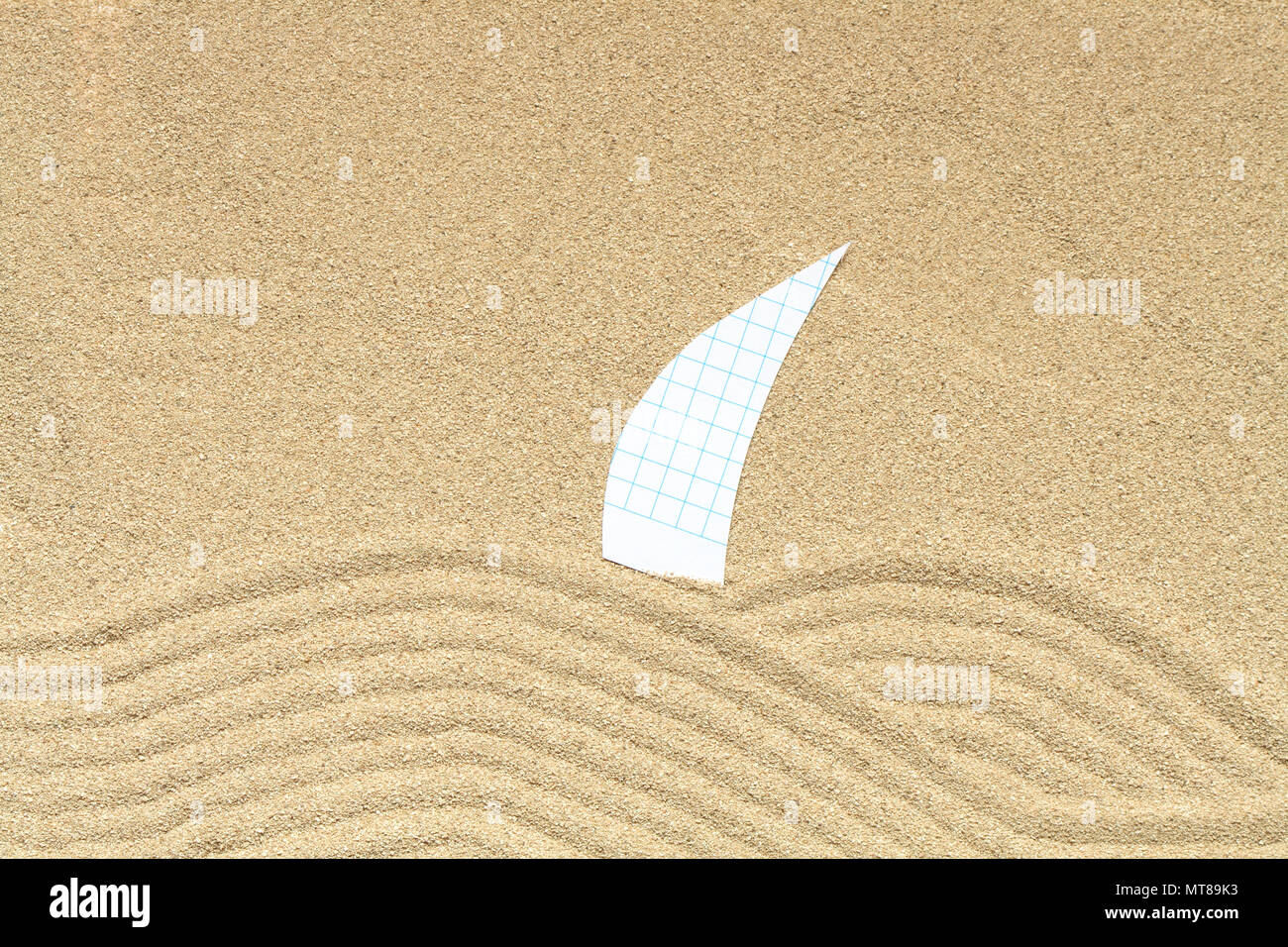 Paper sail lying on sand background with drawing waves Stock Photo