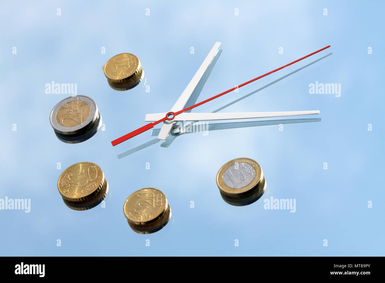 Clock hands and few euro coins lying on mirror background with blue sky and clouds reverberation Stock Photo