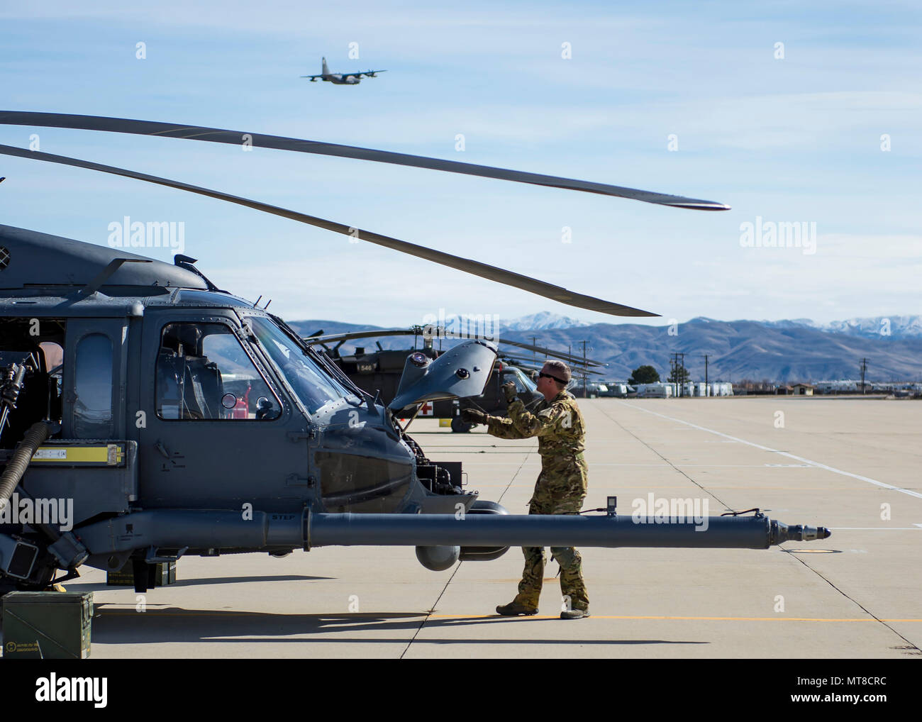 An Airman With The 943rd Rescue Group Performs A Pre Flight Inspection On An Hh 60g Pave Hawk Helicopter As Hc 130j Combat King Ii Flies Over Head March 3 17 At Gowen Field Idaho