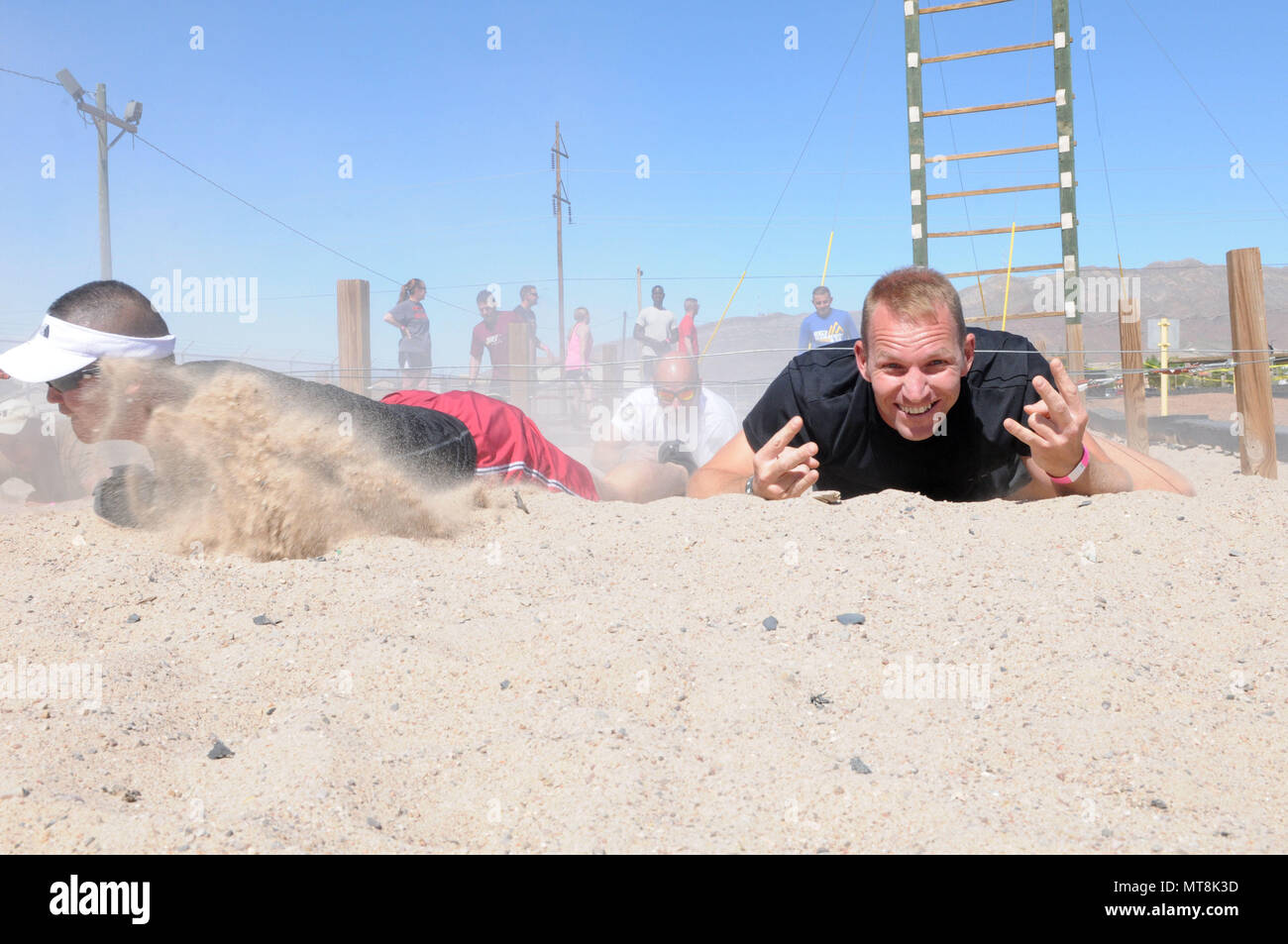 A competitor in the Fort Bliss Old Ironsides Mud Challenge crawls through a sand pit at the air assault course May 12, 2018 on Fort Bliss, Texas. The four-mile course was designed to promote physical fitness while also allowing the community to come together and have fun. (U.S. Army photo by Pfc. Christina Westfall) Stock Photo