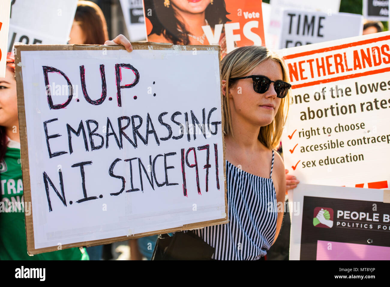 Belfast, Northern Ireland. 28/05/2018 - A woman holds a placard with the message "DUP [Democratic Unionist Party].  Embarrassing NI [Northern Ireland] sine 1971".  Around 500 people gather at Belfast City Hall to call for the decriminalisation of abortion in Northern Ireland.  It comes the day after a referendum held in the Republic of Ireland returned a substantial "Yes" to removing the 8th amendment to the constitution, which gives equal right of life to both the mother and baby, effectively banning abortion in all circumstances. Stock Photo