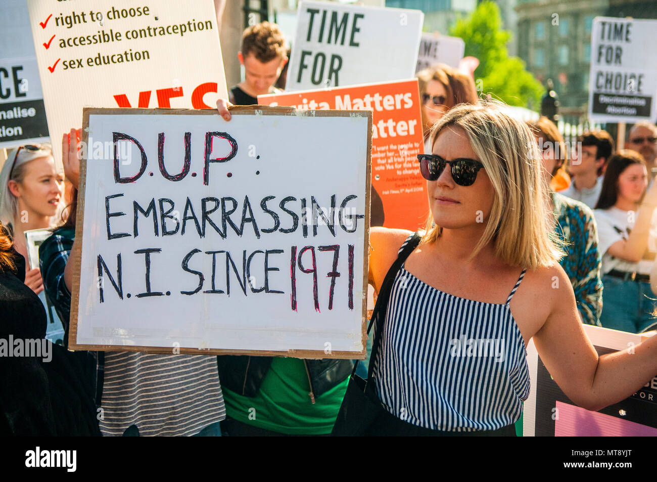 Belfast, Northern Ireland. 28/05/2018 - A woman holds a placard with the message 'DUP [Democratic Unionist Party].  Embarrassing NI [Northern Ireland] sine 1971'.  Around 500 people gather at Belfast City Hall to call for the decriminalisation of abortion in Northern Ireland.  It comes the day after a referendum held in the Republic of Ireland returned a substantial 'Yes' to removing the 8th amendment to the constitution, which gives equal right of life to both the mother and baby, effectively banning abortion in all circumstances. Stock Photo