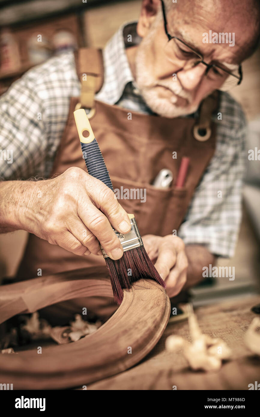 elderly carpenter uses a brush on an unfinished chair Stock Photo