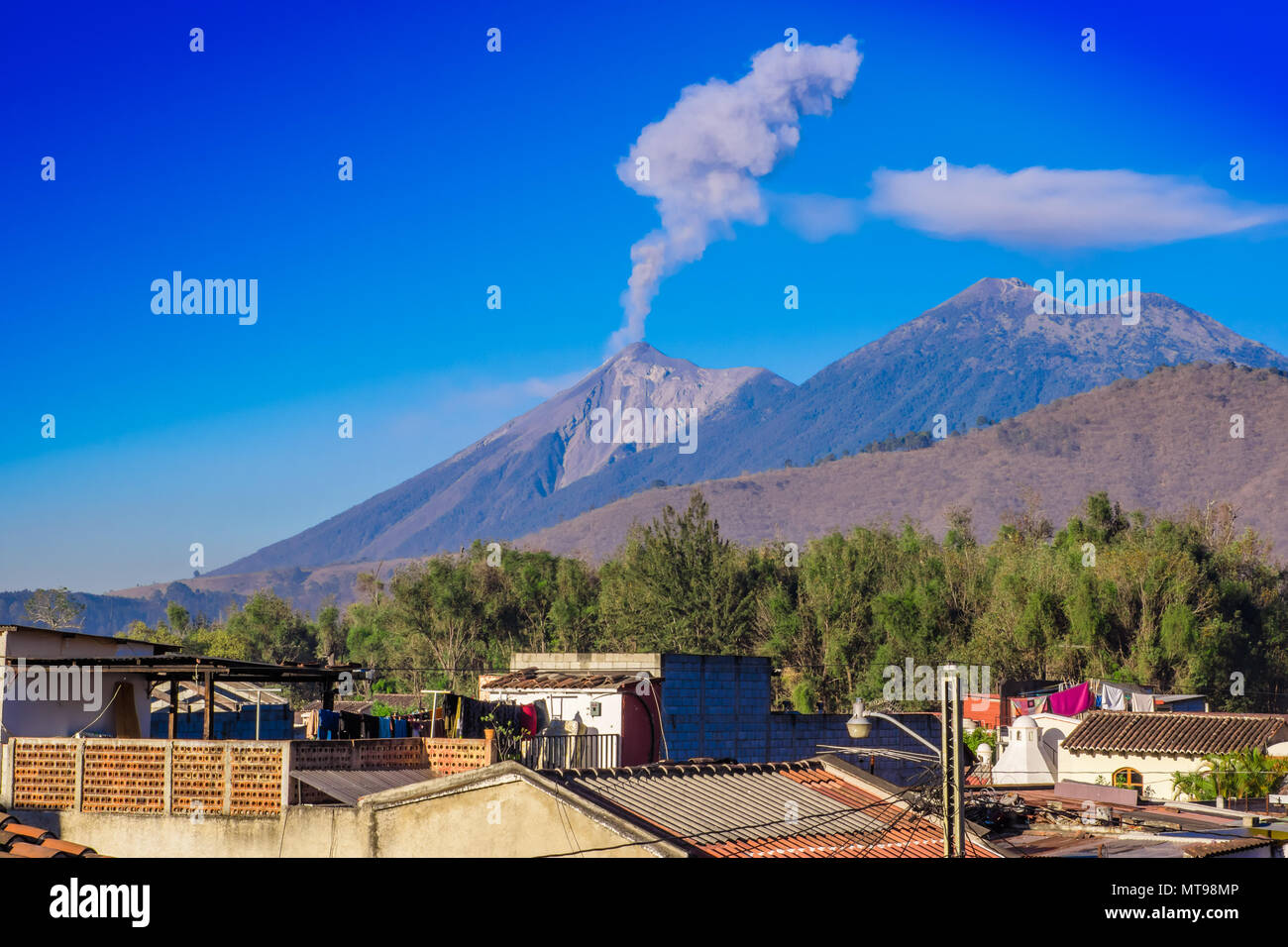 Beautiful landscape of huge mountain in process of aruption with a column of ash, view from the rooftops of the building in Antigua city in gorgeous sunny day and blue sky Stock Photo