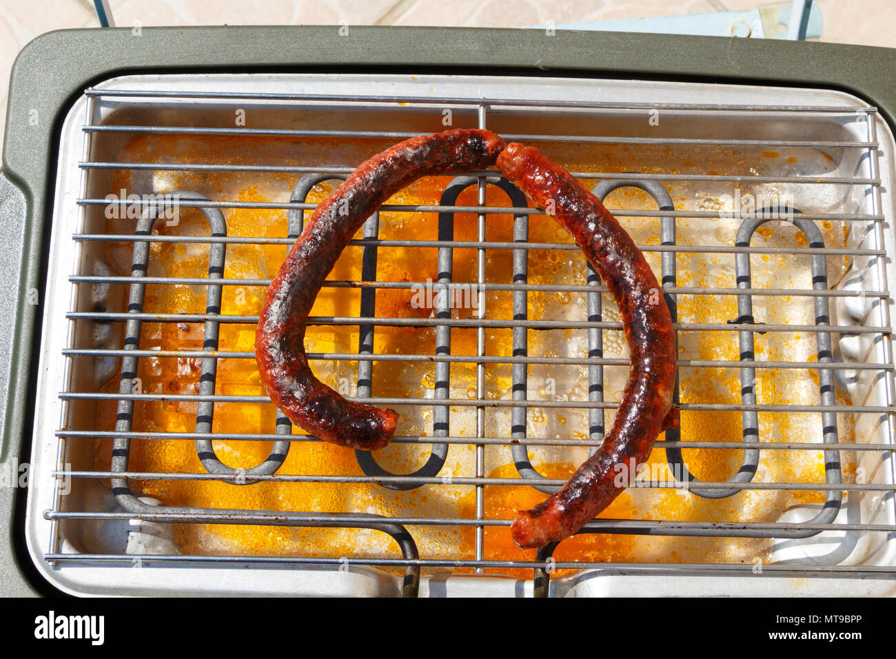 Two cooked merguez on the rack of an electric barbecue Stock Photo