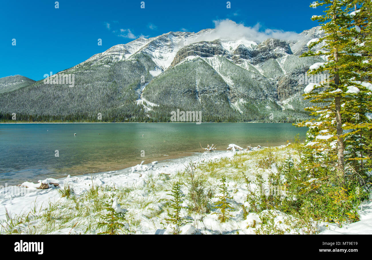 Pristine Kananaskis country in the Canadian Rockies. Snow covers the mountains and trees on the lake shore. Turquoise waters. Blue sky. First snow. Stock Photo