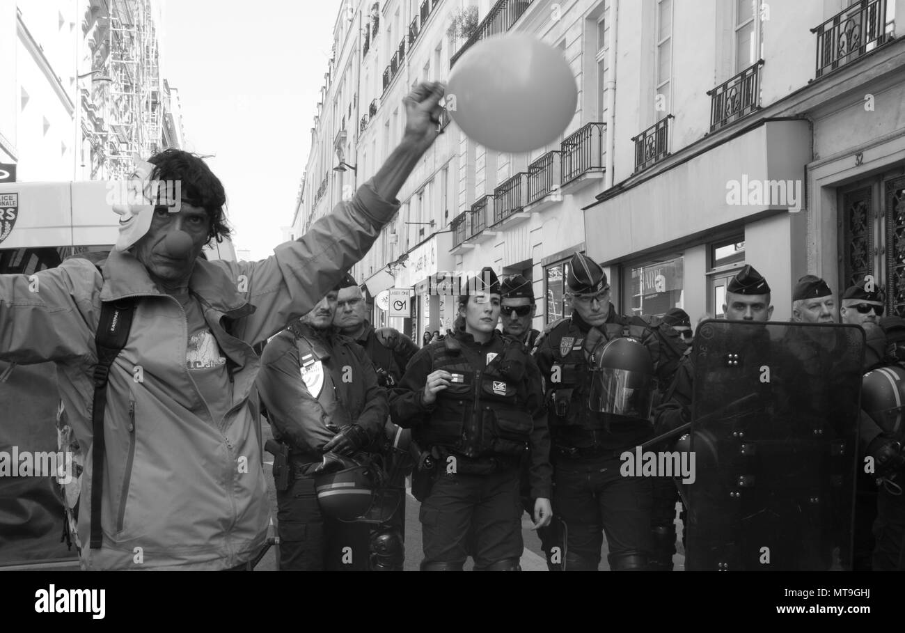 A protestor dressed up as a clown with a balloon stands next to French riot police Stock Photo