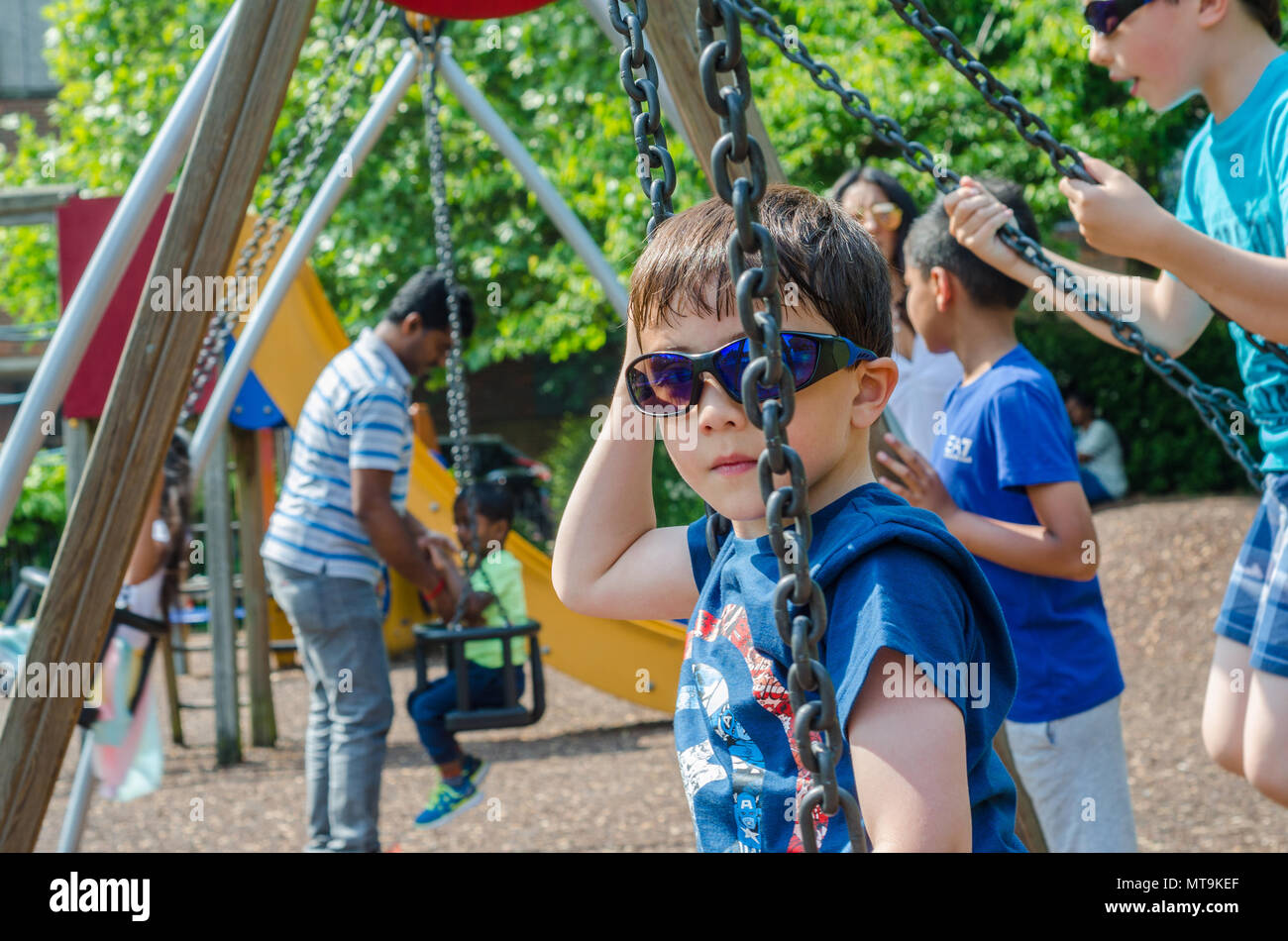 A young boy play on swings in the children's playground in Bachelors Acre in Windsor, UK. Stock Photo