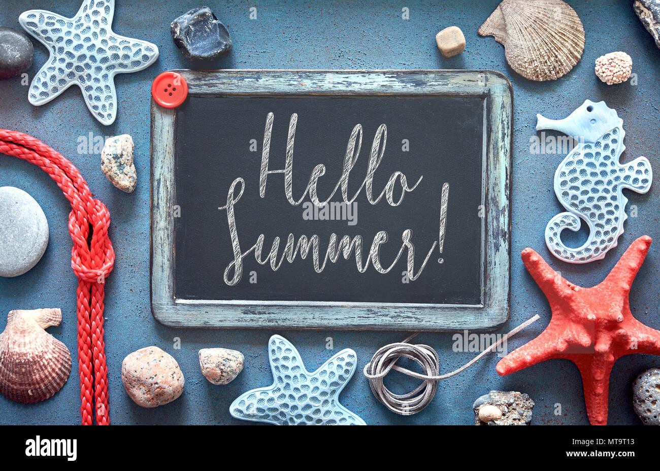 Blank blackboard with sea shells, rope and star fish on blue structured background, text 'Hello Summer' Stock Photo