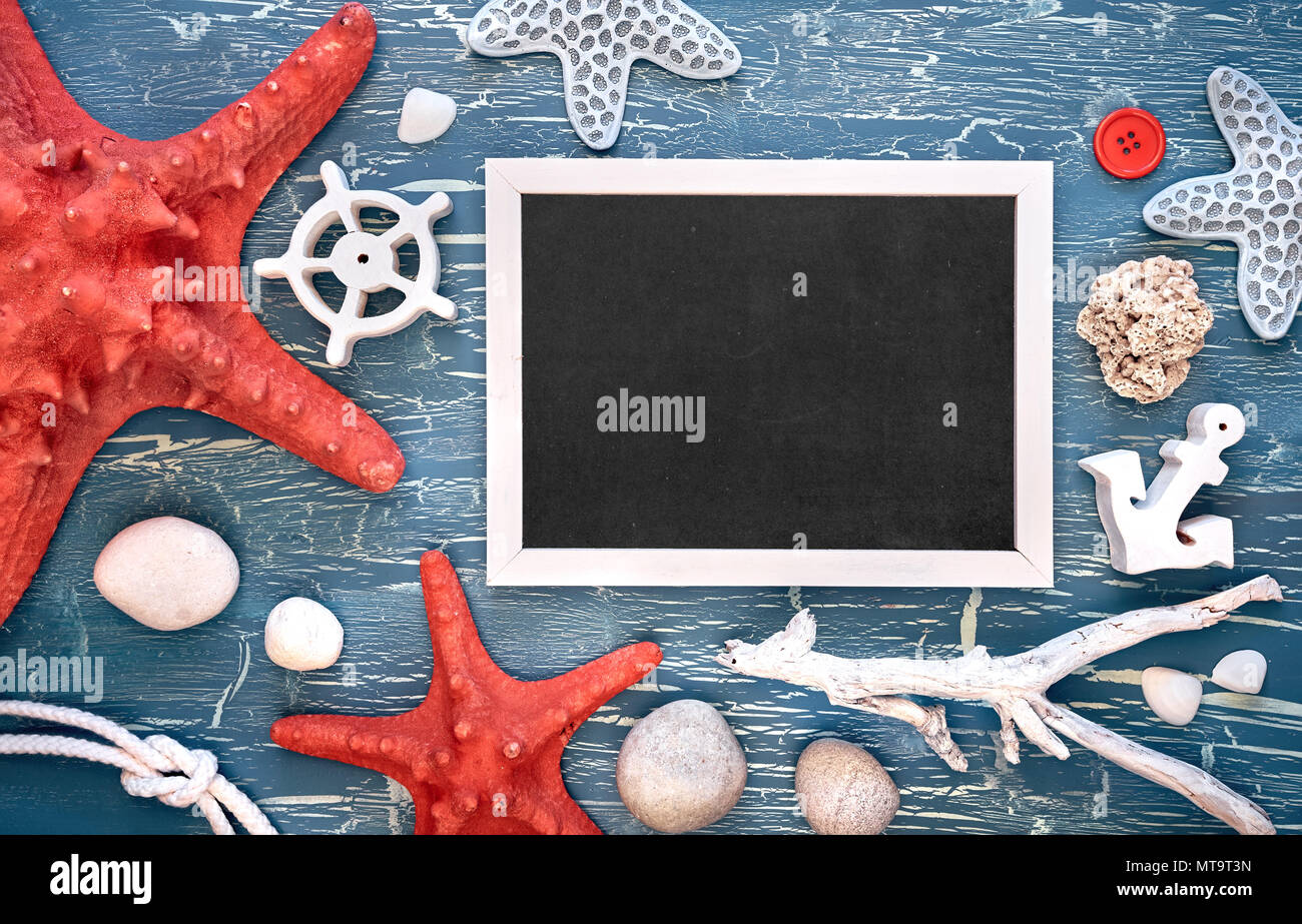 Blank blackboard with sea shells, stones, rope and star fish on blue wooden background, text space Stock Photo