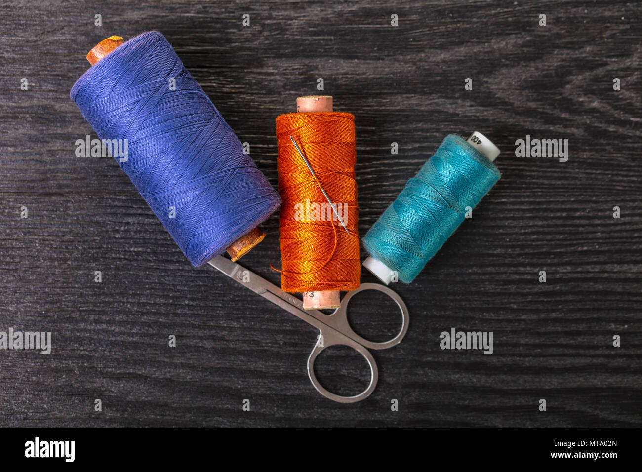 colored threads and scissors on a black wooden background Stock Photo