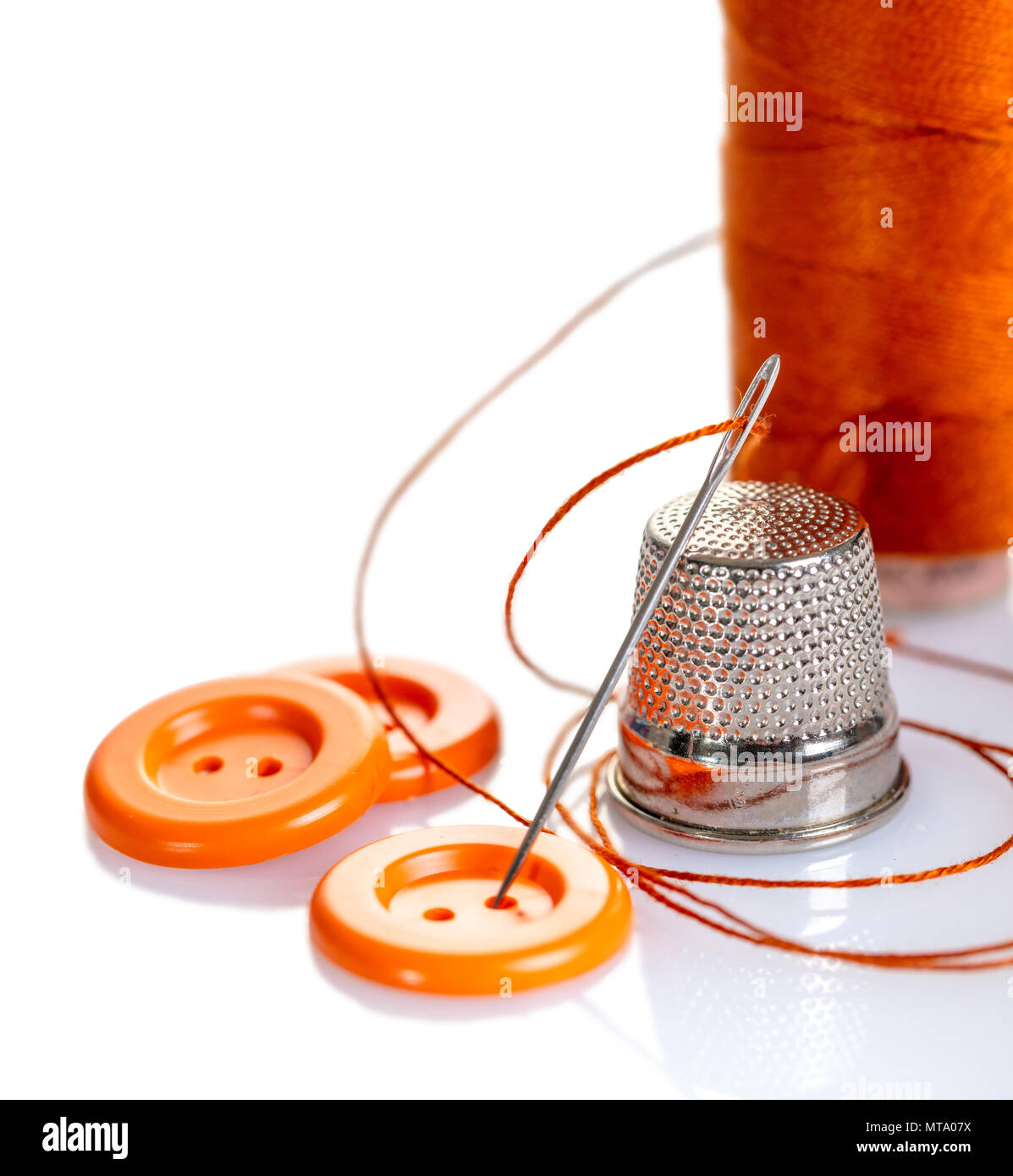 Needle with orange thread and buttons on a white background Stock Photo