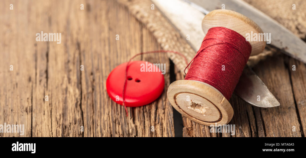 red thread with buttons and scissors, wooden background Stock Photo