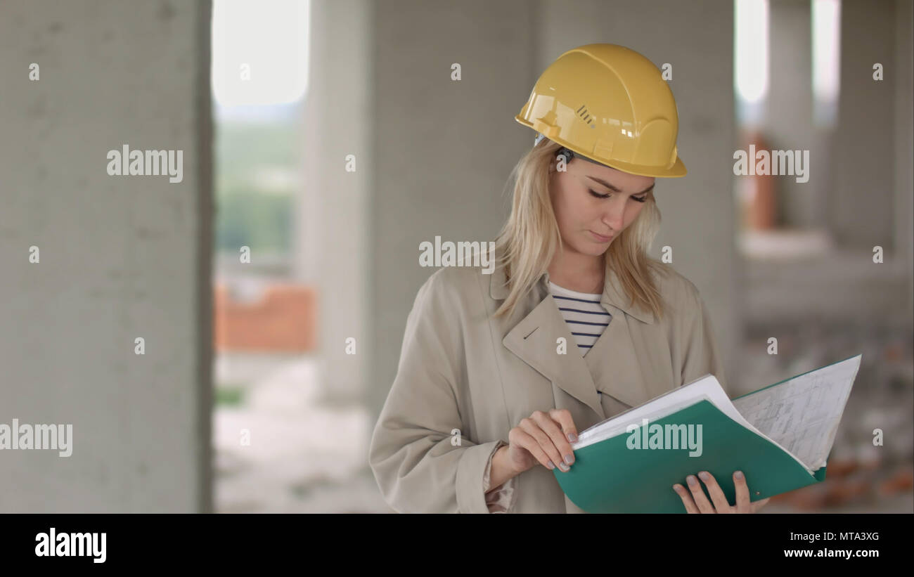 Young female architect construction engineer at a construction site eximaining documents Stock Photo