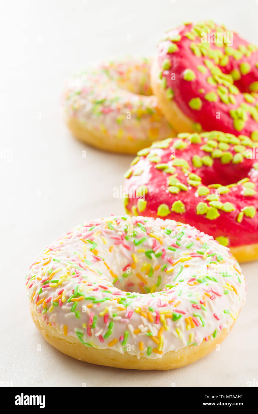 Sweet sprinkled donuts on white kitchen table. Stock Photo