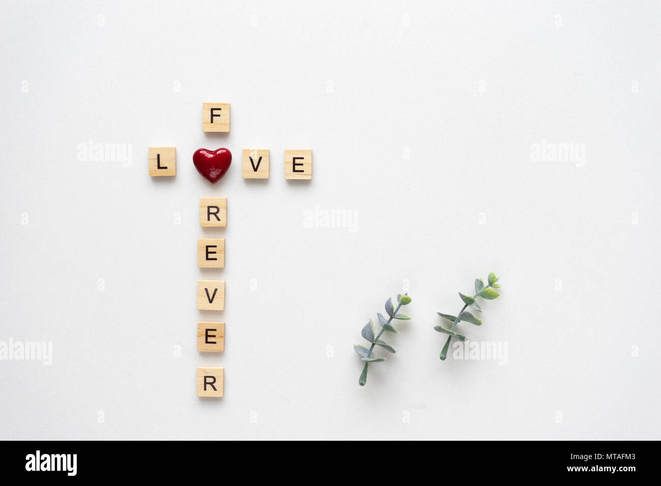 Wooden letters spelling love for ever, with oregano branches on white