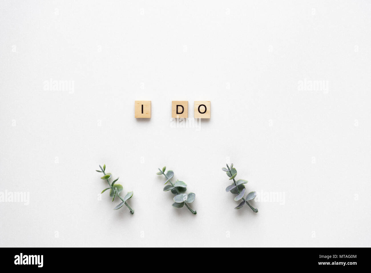 Wooden letters spelling I do with oregano branches on white marble. Top
