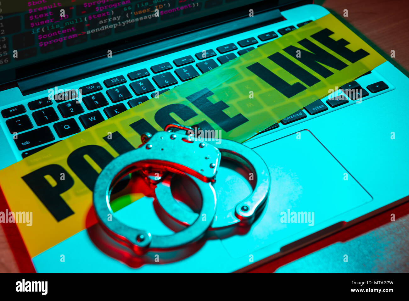 A pair of handcuffs and police line tape sit atop a laptop keyboard. Technology/cyber crime concept. Stock Photo