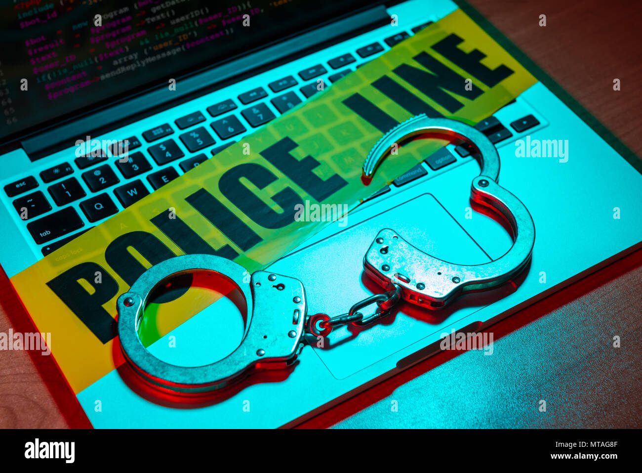 A pair of handcuffs and police line tape sit atop a laptop keyboard. Technology/cyber crime concept. Stock Photo
