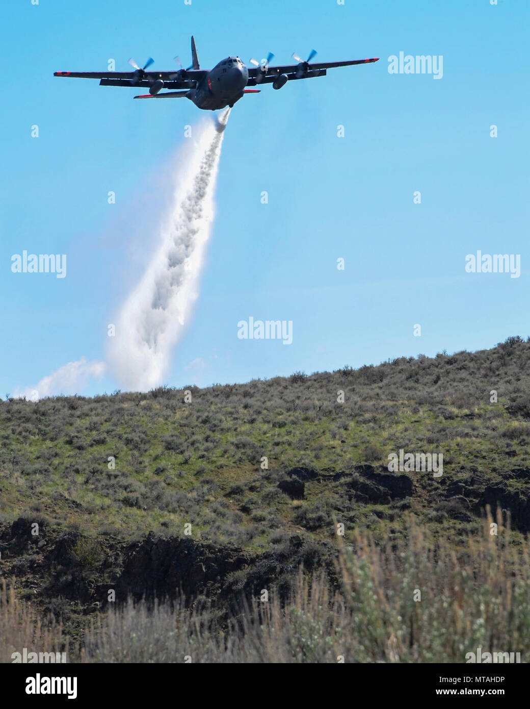 A C130h aircraft loaded with the MAFFS (Modular Airborne Fire Fighting System) from the 152nd Airlift Wing of Reno, Nevada drops a water line while training to contain wildfires just outside Boise, Idaho. April 21, 2017. More than 400 personnel of four C-130 Guard and Reserve units — from California, Colorado, Nevada and Wyoming, making up the Air Expeditionary Group — are in Boise, Idaho for the week-long wildfire training and certification sponsored by the U.S. Stock Photo