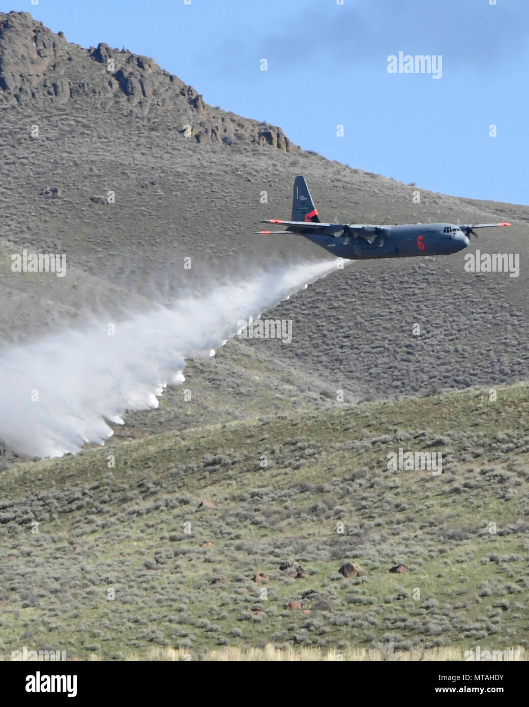 A C130J aircraft loaded with the MAFFS (Modular Airborne Fire Fighting System) from the 146th Airlift Wing of Port Hueneme, California drops a water line while training to contain wildfires just outside Boise, Idaho. April 21, 2017. More than 400 personnel of four C-130 Guard and Reserve units — from California, Colorado, Nevada and Wyoming, making up the Air Expeditionary Group — are in Boise, Idaho for the week-long wildfire training and certification sponsored by the U.S. Stock Photo