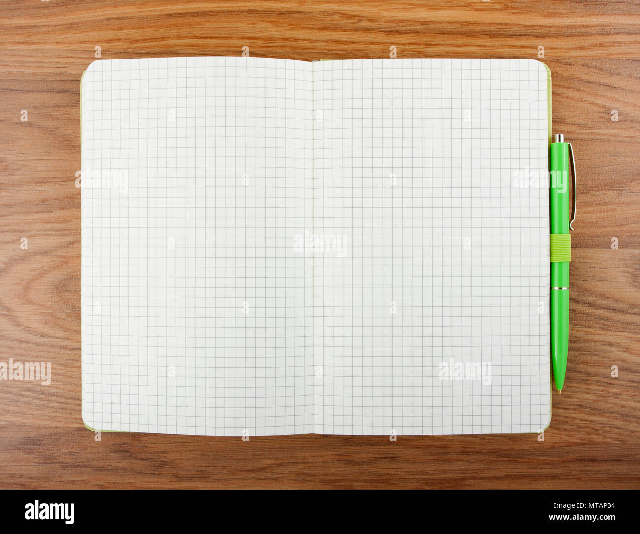 Open blank checked notebook with green pen on a table Stock Photo