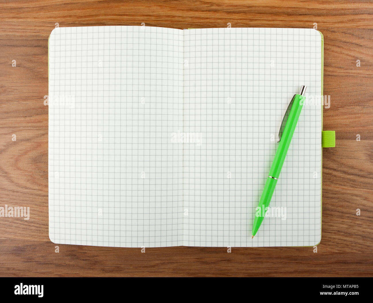 Open blank checked notebook with green pen on a table Stock Photo
