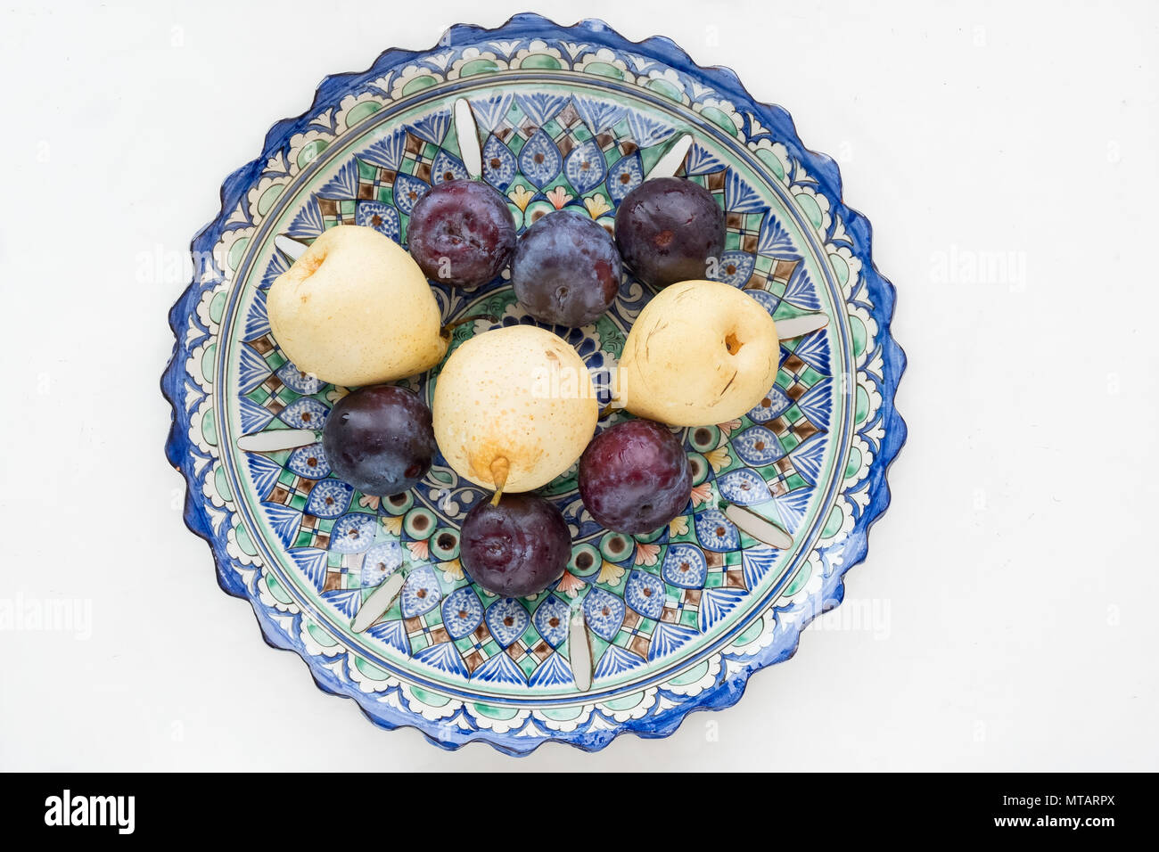 Pears and plums in an Uzbek bowl. Top view on a white background. Stock Photo