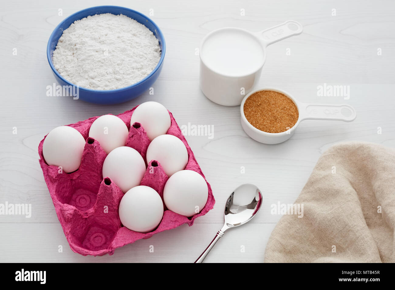 Baking ingredients on white wooden kitchen table. White eggs in pink