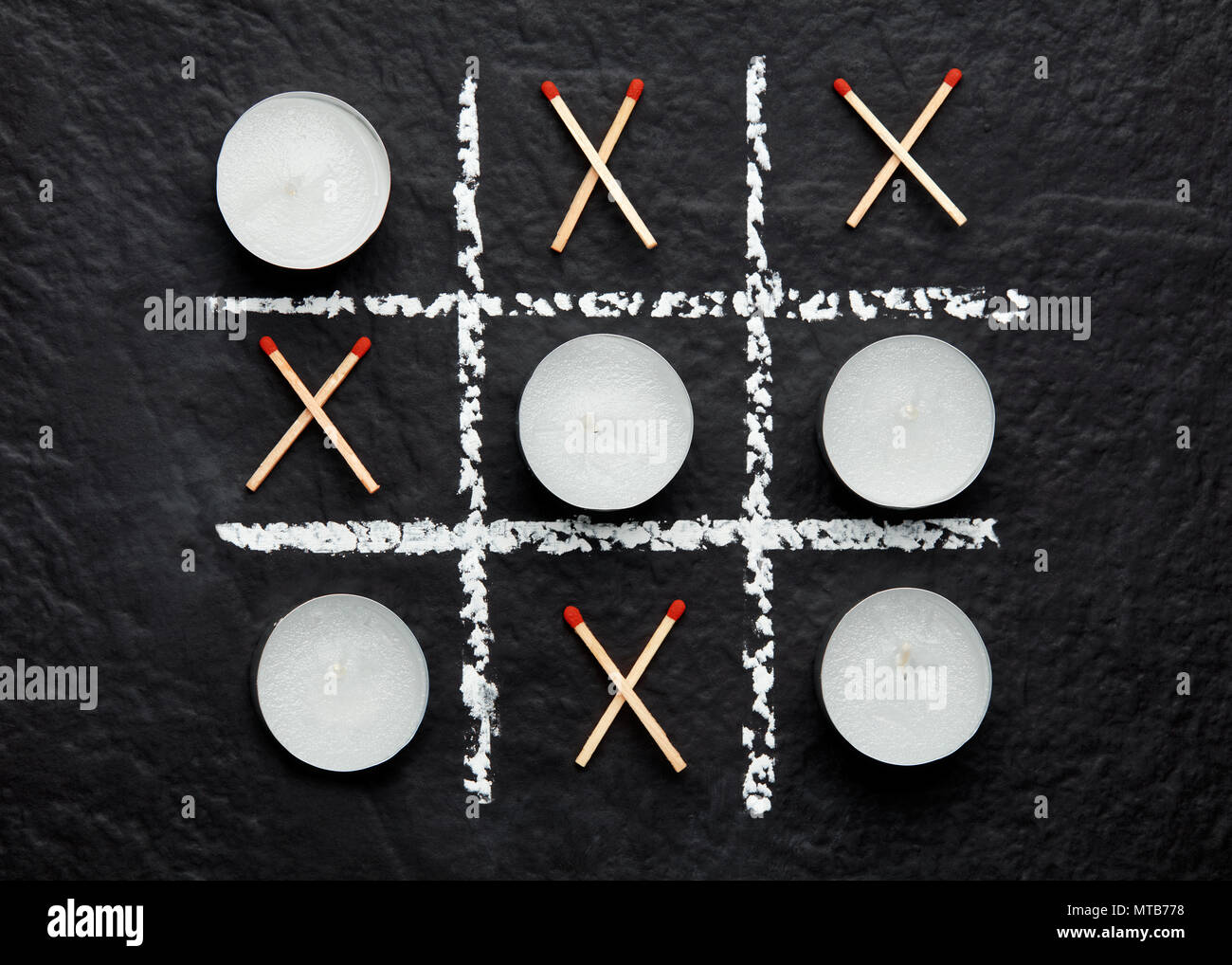 Tic tac toe xo game with candles and matches on textured black surface. Concept of do or die and life or death. Top down close up view. Stock Photo