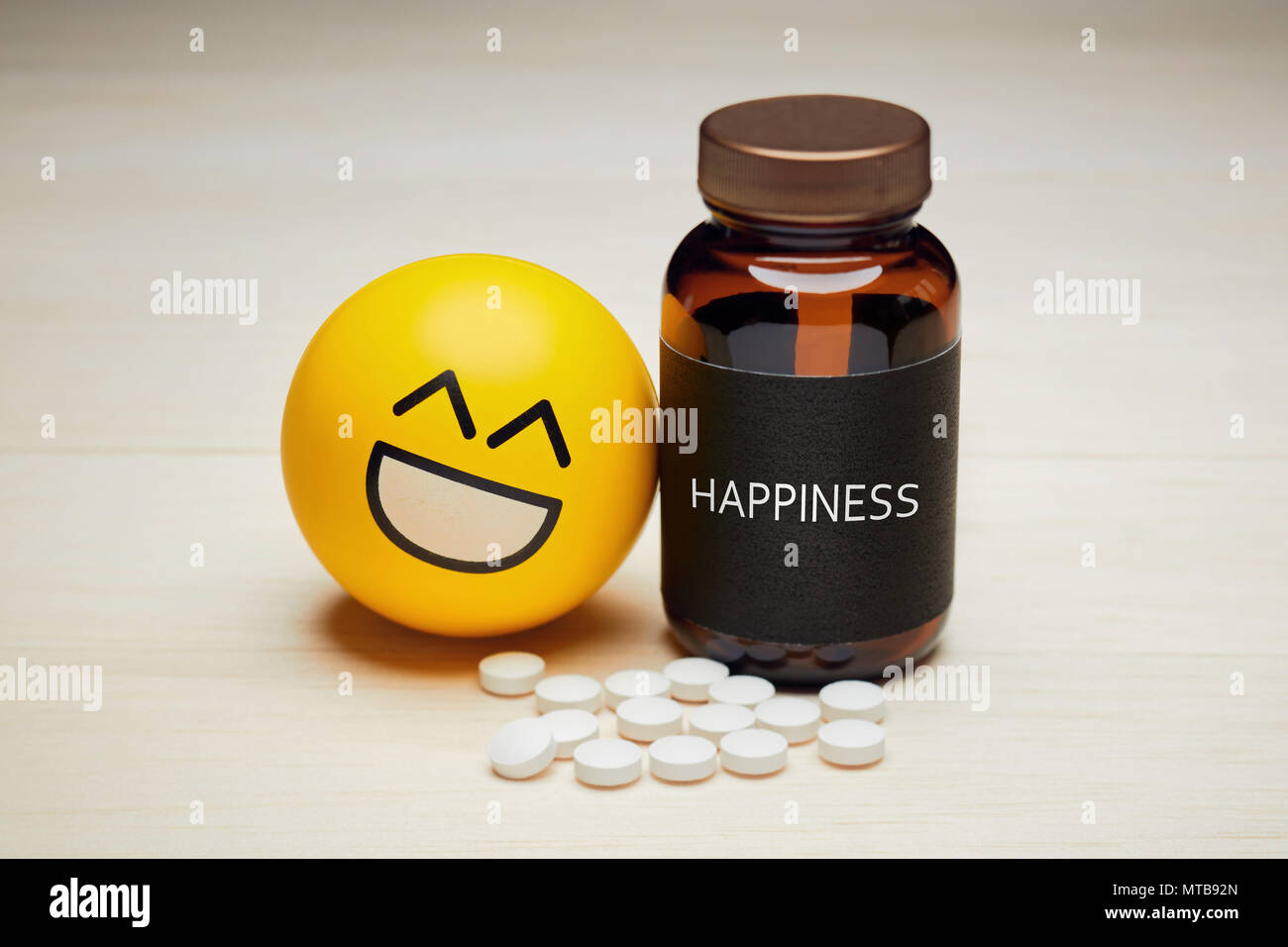 Anti depressant drug use and happiness concept. Yellow smiling emoji reclined to a drug container with a black label written happiness on it. Heap of  Stock Photo