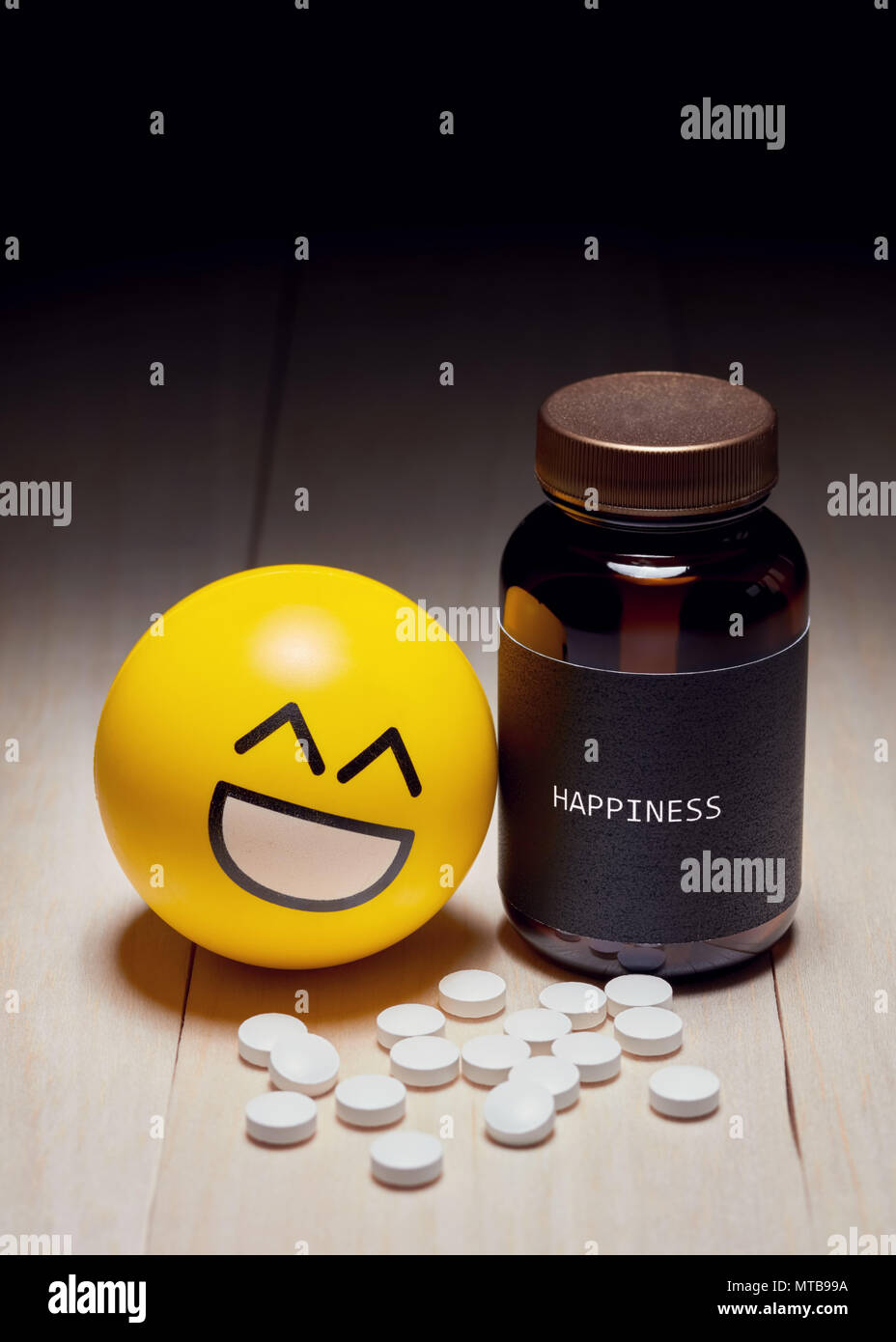 Anti-depressant drug use and happiness concept. Yellow smiling emoji reclined to a drug container with a black label written happiness on it. Editoria Stock Photo