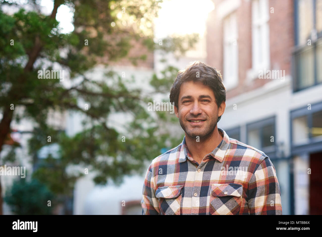 Portrait of a casually dressed young man smiling while standing by himself on a street in the city on a sunny afternoon Stock Photo
