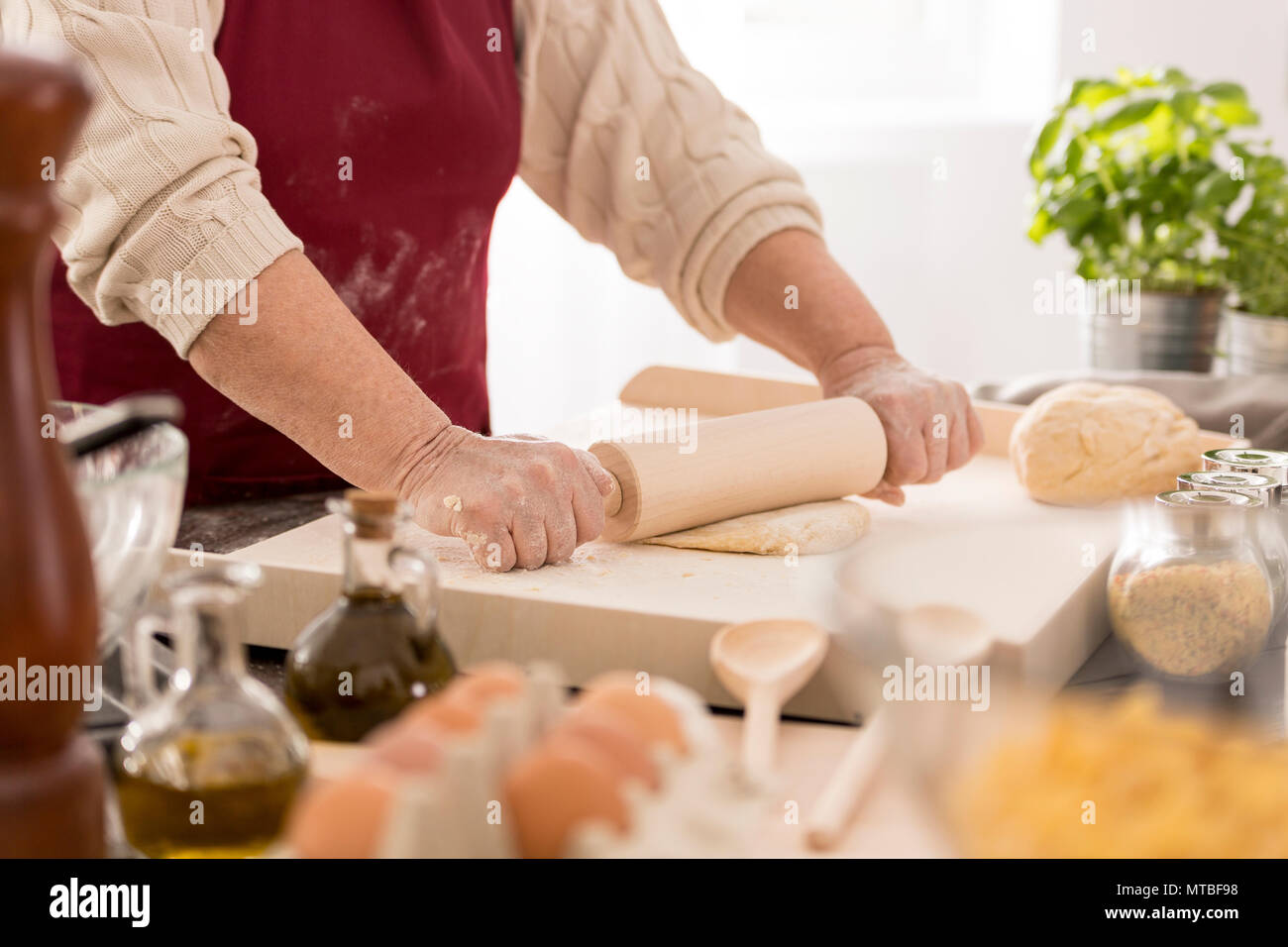 Old woman rolling the dough on a pastry board in a kitchen Stock Photo
