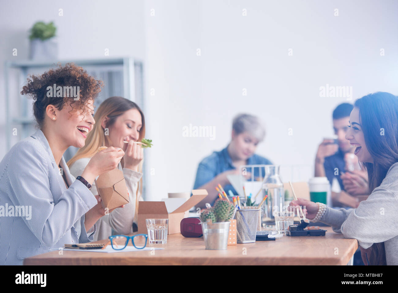 Caucasian employees eating lunch with their mulatto coworker Stock Photo